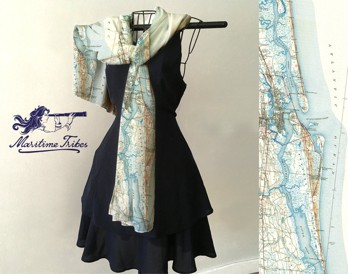 A scarf with a vintage topographic map design, featuring shades of blue and beige, displayed on a mannequin wearing a black dress.