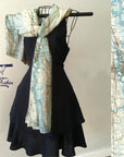 A scarf with a vintage topographic map design, featuring shades of blue and beige, displayed on a mannequin wearing a black dress.