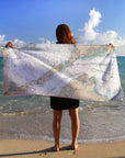 A person standing on a beach holding a white nautical chart towel with a map of Woods Hole to Cuttyhunk.